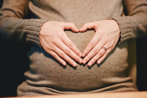 Pregnant mom hands formed heart shape on top of tummy