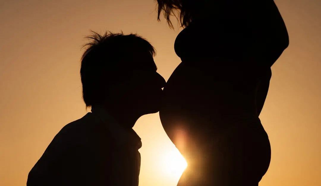 Silhouette of a man kissing his pregnant woman