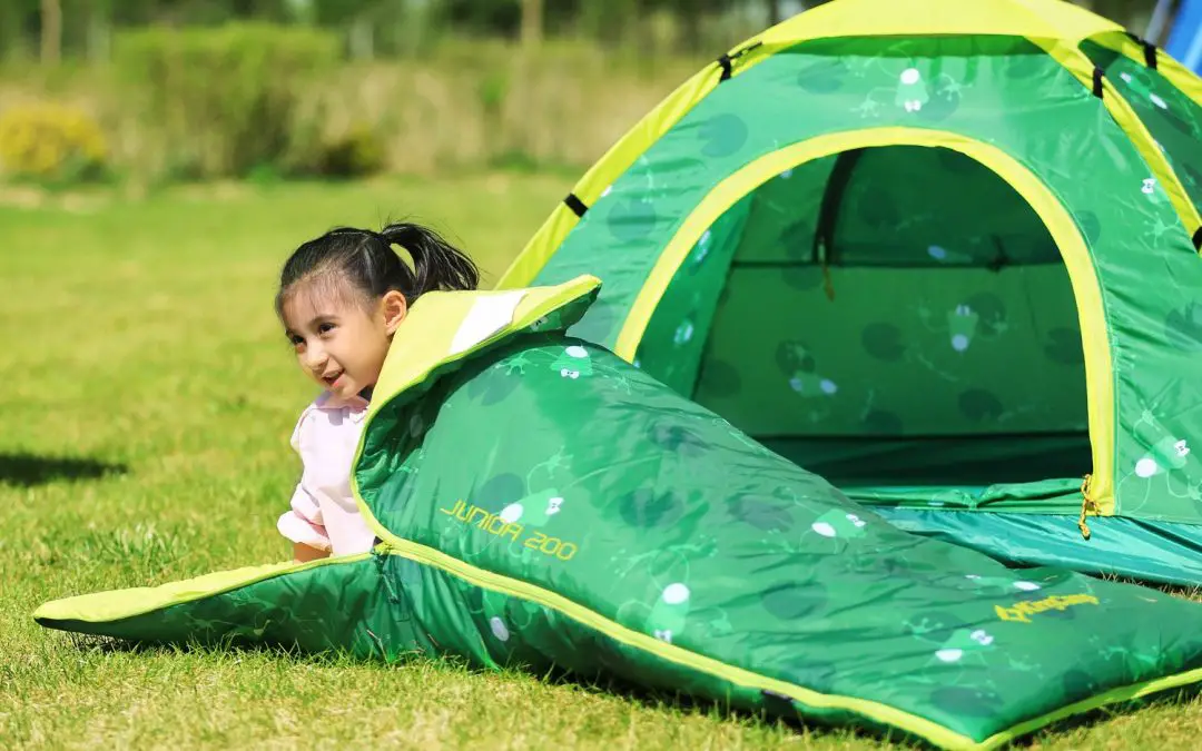 Toddler on a green sleeping bag in front of her green tent