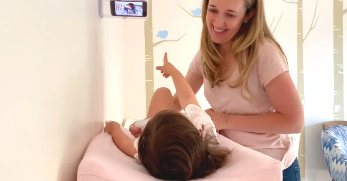 Image of a smiling mom and her baby pointing at the diapertainment mounted on the wall