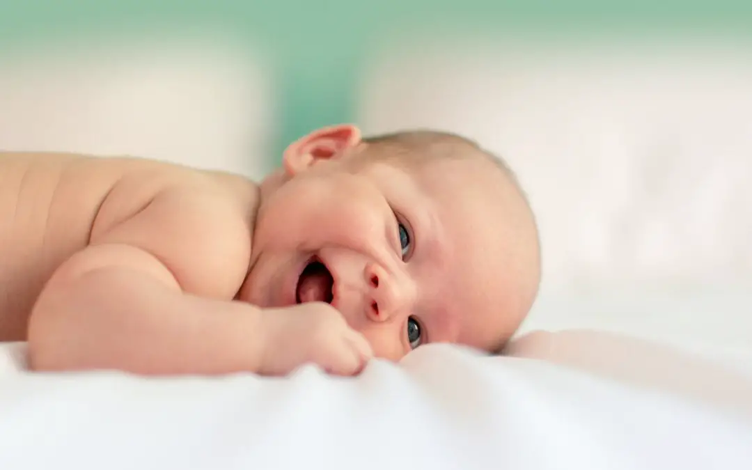 naked baby lying face down on the mattress smiling