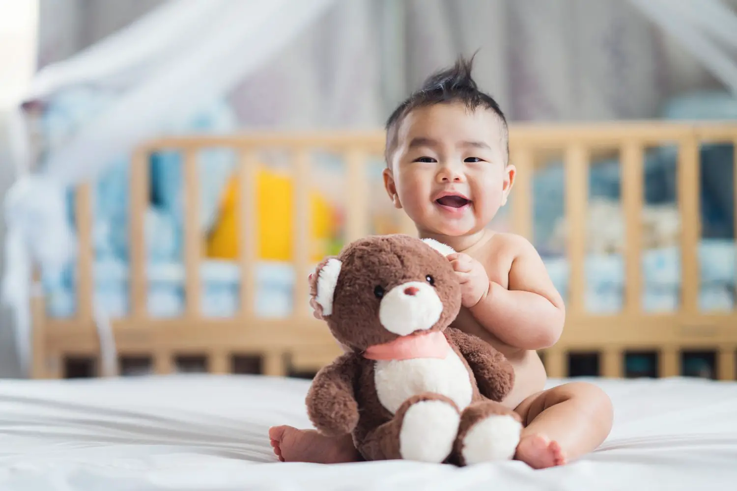 sitting baby holding a brown teddy